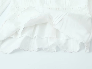 Détail du chemisier blanc montrant la broderie ajourée et l'ourlet plissé ondulé