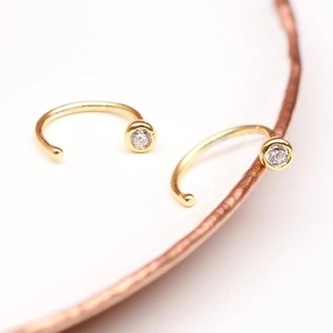 Macro detail of gold-plated C-shaped nose ring featuring a round clear zircon stone