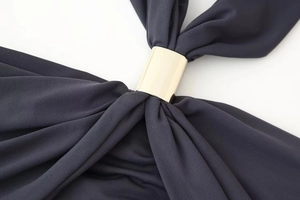 Détail de tissu gris foncé froncé par un anneau métallique doré sur une robe licou