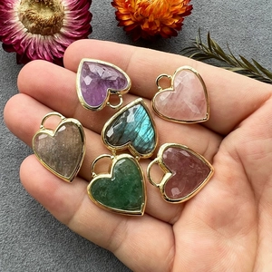 Hand holding six heart-shaped natural crystal pendants with gold metal frames