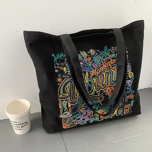Detail of black canvas tote featuring colorful street art embroidery and wide strap