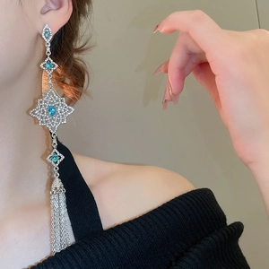 Detail of luxury silver needle earrings featuring blue crystal and long chain tassels