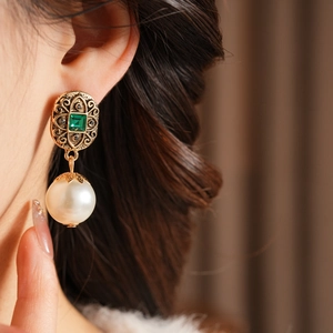 Dettaglio di orecchini vintage con pietre verdi e perle indossati da modella