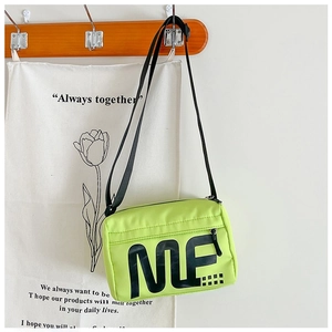 Détail du sac bandoulière en nylon vert fluo avec imprimé ME noir sur un crochet en bois