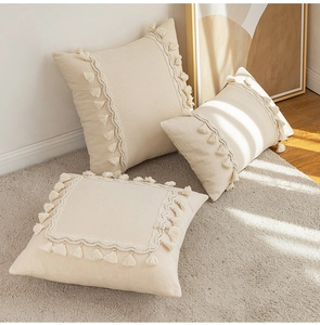 Detailed view of beige fringe pillow covers on rug showing textured cotton fabric