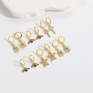 Flat lay of gold turtle and evil eye earrings with colorful zircons on white stone