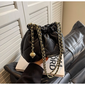 Detail of black quilted leather bucket bag with gold chain strap and spherical charm ornament