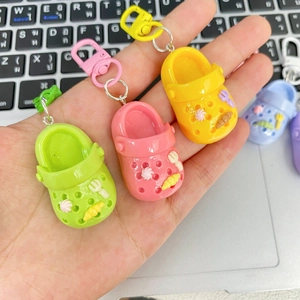 Cute colorful mini clog shoe keychains in pink, yellow and green held over a laptop keyboard