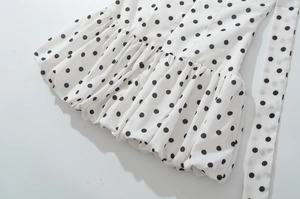 Détail d'une robe blanche à pois noirs avec texture plissée et ceinture assortie