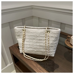 Detailed macro view of white textured tote bag with elegant gold-tone chain strap