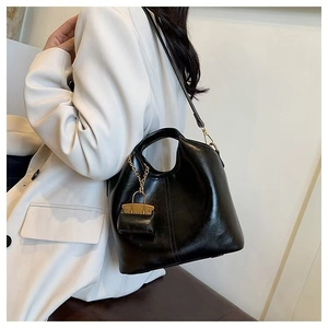 Detailed view of black oil wax leather bucket bag with mini charm on a white blazer model