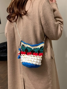 Handmade cherry knit bucket bag with pearl strap worn by a model in a minimal indoor setting