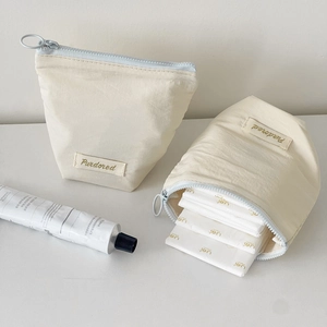 Detail view of cream-colored cosmetic bag with ring zipper and interior storage capacity