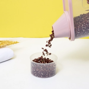 Clear plastic food storage container with pink lid pouring red beans into a measuring cup