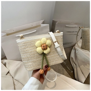 Macro detail of hand-woven straw bucket bag with floral accent and white leather strap