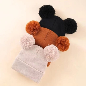 Detailed knit texture of three kids' double pom-pom beanies in multiple colors