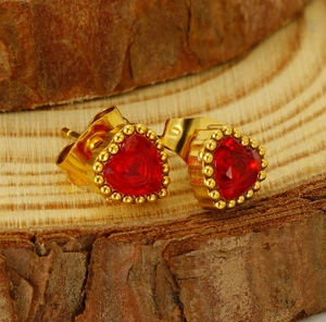 Close-up of heart-shaped red crystal stud earrings on natural wood texture