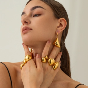 Dettaglio di anelli geometrici in oro 18 carati e orecchino a triangolo su una modella
