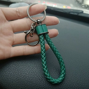 Close-up of a green woven leather ball keychain with gunmetal ring in a car interior