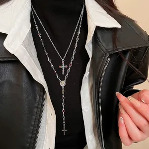 Double-layered silver necklace with colorful cross pendant and saint medal on a model