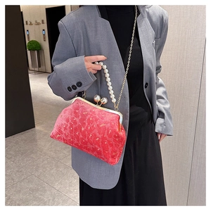 Close-up of a red velvet shell bag featuring pearl handle and gold metallic clasp
