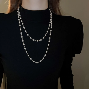 Détail d'un collier de perles artificielles multicouches avec chaînes dorées sur haut noir