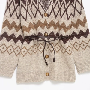 Knit cardigan with geometric patterns, waist belt, and four brown buttons on cream fabric