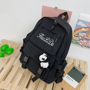 Detail of black canvas backpack with panda pendant and buckle straps on wooden background