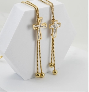 Close-up of 18K gold plated cross pendant with rhinestones on white geometric stand