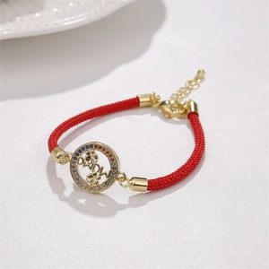 Détail d'un bracelet tissé rouge avec pendentif doré et zircons colorés sertis