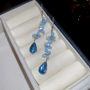 Close-up of sparkling blue butterfly earrings with water drop pendants on velvet base