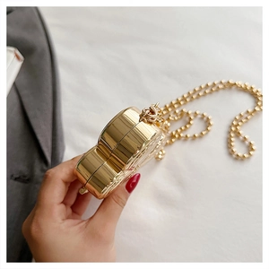Detail of a golden heart-shaped mini clutch bag with metallic chain strap held by hand