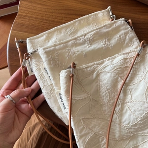 Detailed view of floral embroidery on a cream cotton crossbody bag with leather strap