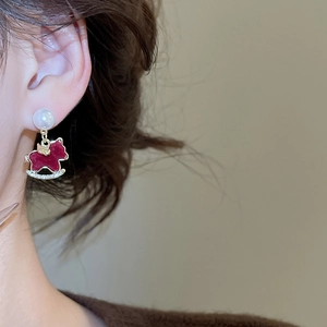 Close-up of red rocking horse earrings with pearl stud and rhinestones worn by a model