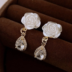 Macro view of white rose earrings with gold metal buckle and teardrop zircon pendant