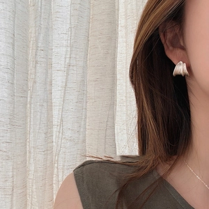 Close-up of silver C-shaped earrings with vertical textured ripples on female model