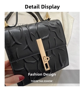 Detail of black embossed leather handbag showing intricate branch texture and gold buckle