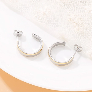 Polished C-shape hoop earrings with gold inlay accent displayed on a white ceramic tray