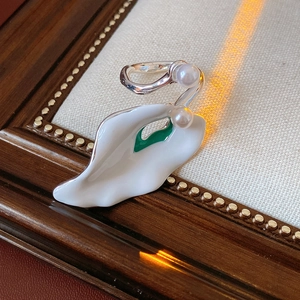 Detailed close-up of white enamel petal earrings with pearls and green accents on silver