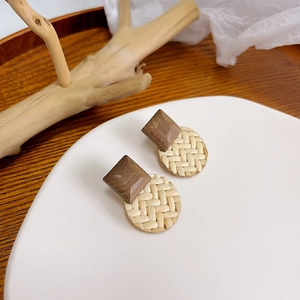 Macro shot of handmade woven round grass and rhombus wood stud earrings on a wooden tray
