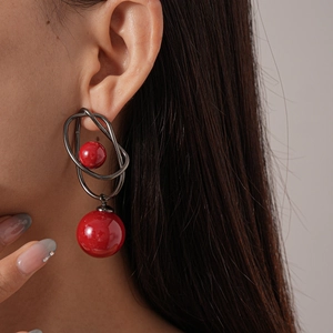 Model wearing acrylic geometric twisted earring with glossy red spheres on a light grey background