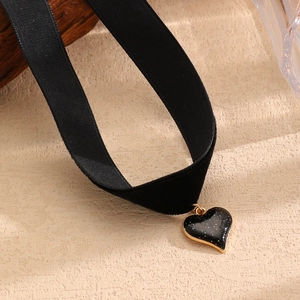 Dettaglio del ciondolo a cuore in smalto nero con base dorata su choker di velluto