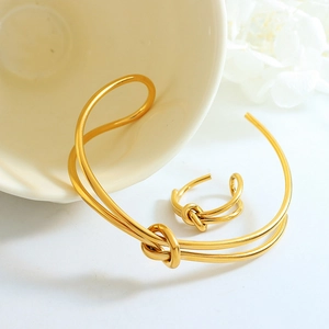 Golden double-layer knotted jewelry set with open bangle and ring on minimalist background