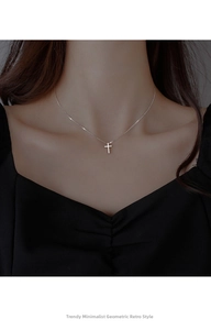 Close-up of minimalist silver cross necklace worn on a collarbone with a delicate chain