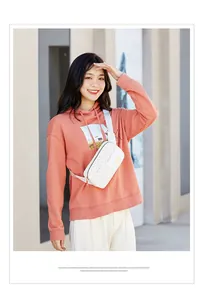 Outdoor model shot of white geometric patterned crossbody bag with gold metal plaque detail