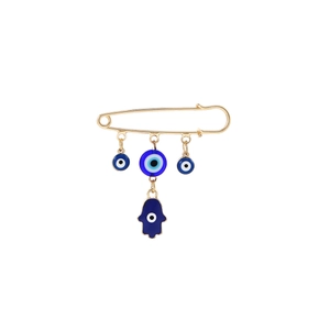 Detailed view of gold brooch with blue evil eye charms and Hamsa hand pendant on white base