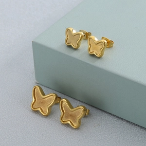 Macro shot of gold butterfly stud earrings with matte texture on green geometric blocks