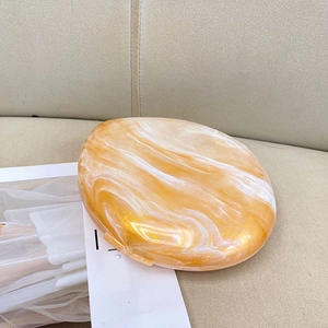 Top view of a round amber acrylic clutch bag with marble texture on beige fabric