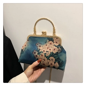 Detail view of floral fabric handbag with gold metal clasp and chain strap held by hand