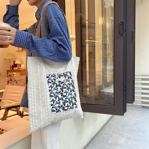 Detail of white textured canvas tote bag featuring a blue butterfly pocket and lace texture